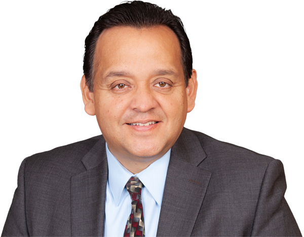 A man in a dark suit, light blue shirt, and patterned tie is smiling at the camera against a plain white background.